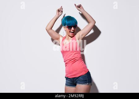 Giovane donna gioiosa in abiti casual in piedi su sfondo bianco con ombra mentre ballare alzando le mani Foto Stock