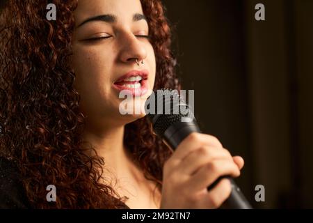 Vista laterale della giovane cantante femminile in camicia nera con capelli ricci che cantano la canzone nel microfono durante le prove Foto stock Alamy