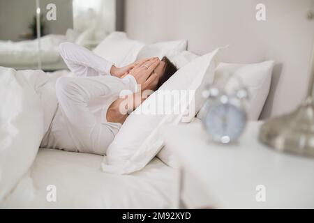 Donna stressata con sveglia sdraiata a letto a casa Foto Stock