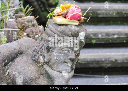 Offerta religiosa balinese (canang sari) su una statua di pietra. Foto Stock