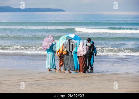 Donne musulmane e un giovane uomo che guarda verso il mare sulla spiaggia di Bali, Indonesia Foto Stock