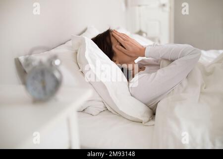 Bruna donna stanca sdraiata a letto a casa al mattino Foto Stock