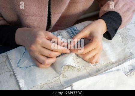 Primo piano delle mani di una donna che cucia una maglietta nazionale Ucraina ricamata Foto Stock