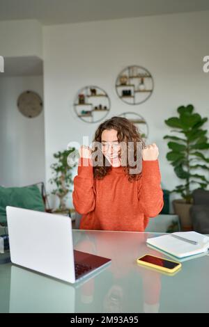 Felice giovane donna che guarda il laptop vincere online, verticale. Foto Stock