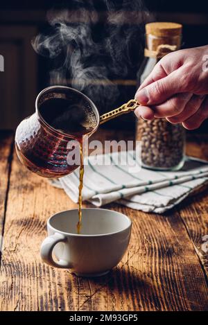 Versare il caffè turco in una tazza bianca. Vasetto di chicchi di caffè tostati su sfondo Foto Stock