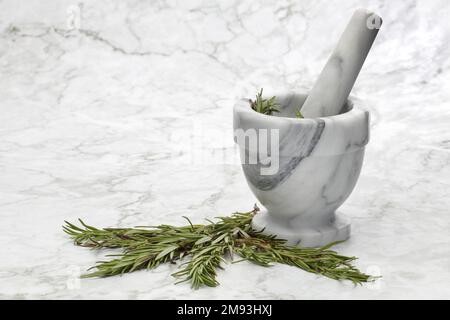 Erbe di rosmarino e un mortaio e pestello su superficie di marmo grigio e bianco Foto Stock