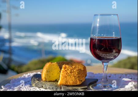 Abbinamento di cibo e bevande portoghesi, bicchiere di vino porto bruno e coccodrillo pastais de bacalhau, servito all'aperto con vista sul blu soleggiato Atla Foto Stock