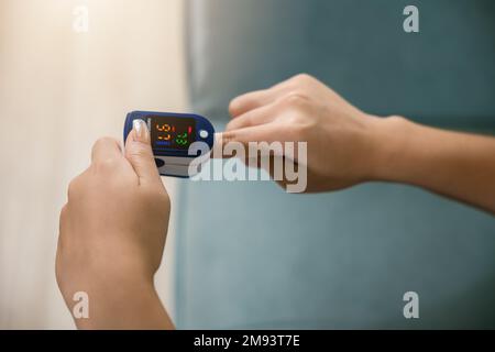 Donna giovane che utilizza il pulsossimetro per monitorare i livelli di ossigeno nel sangue e la frequenza del polso sul dito Foto Stock