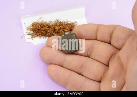 Pezzo di hashish con tabacco su sfondo rosa Foto Stock