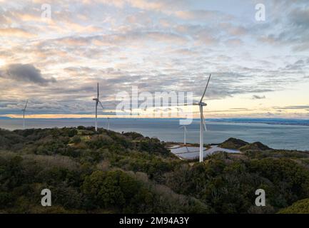 Turbine eoliche su piccola fattoria solare in verde paesaggio di mare al tramonto Foto Stock