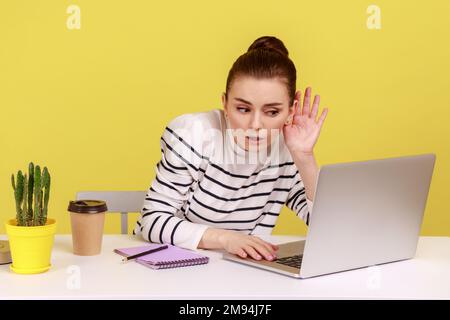 Non ti sento. Donna che tiene il braccio vicino all'orecchio cercando di ascoltare la conversazione segreta durante la videochiamata sul laptop, connessione internet errata, conferenza online. Studio interno girato isolato su sfondo giallo. Foto Stock