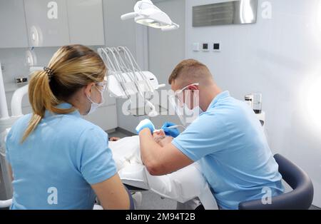 il medico con i guanti blu applica un unguento ai denti del paziente che mostra dove è la placca che deve essere pulita. pulizia e lucidatura dei denti Foto Stock