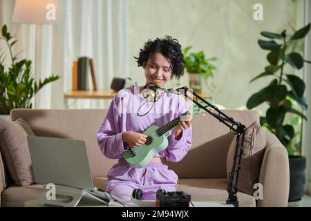 Ragazza giovane sorridente che si registra giocando ukulele e cantando Foto Stock