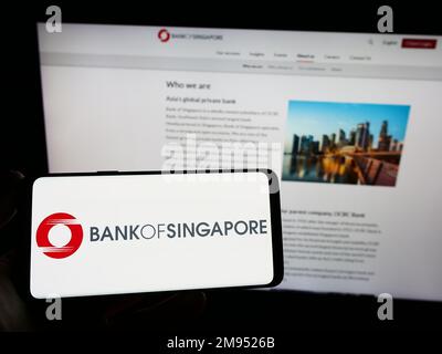 Persona che tiene uno smartphone con il logo della società di servizi finanziari Bank of Singapore sullo schermo di fronte al sito Web. Messa a fuoco sul display del telefono. Foto Stock