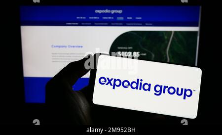 Persona che detiene un telefono cellulare con il logo della società di viaggi online americana Expedia Group Inc. Sullo schermo di fronte alla pagina web. Messa a fuoco sul display del telefono. Foto Stock