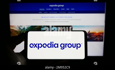 Persona che detiene il cellulare con il logo della società di viaggi online US Expedia Group Inc. Sullo schermo di fronte alla pagina web aziendale. Messa a fuoco sul display del telefono. Foto Stock