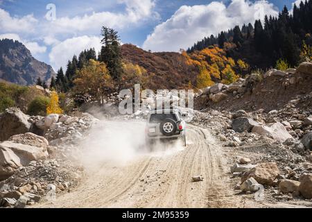 L'auto SUV bianca sale su una strada polverosa nelle montagne autunnali Foto Stock