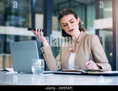 Male matita che nel mio diario subito. una giovane donna d'affari che scrive appunti mentre usa un cellulare in un ufficio. Foto Stock