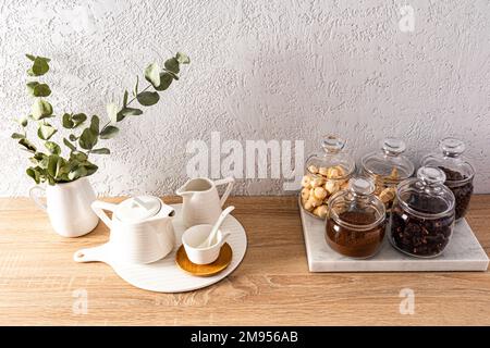 vasetti di vetro con tè, caffè, zucchero su un asse di marmo e articoli da tè sul banco della cucina. parte di un frammento di una cucina moderna Foto Stock