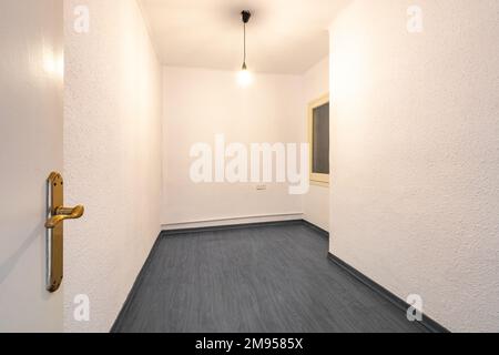 Ingresso ad una spaziosa camera da letto vuota con pareti color crema e pavimenti neri in legno duro. Lampada senza ombra appende dal soffitto, illuminando la stanza Foto Stock