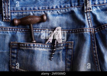 vecchio cavatappi e apribottiglie in una tasca posteriore di jeans blu Foto Stock