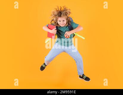 Tutta la lunghezza del salto eccitato del capretto. Ragazzo in uniforme scolastica con zaino che salta su sfondo giallo isolato. Ragazzi che imparano la conoscenza e ragazzi Foto Stock