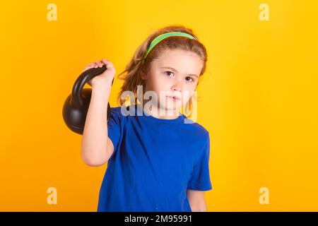 Bambini sportivi, studio isolato ritratto su sfondo giallo. Bambino ragazzo pompare i muscoli bicipiti con Kettlebell. Fitness bambini con manubri. Foto Stock