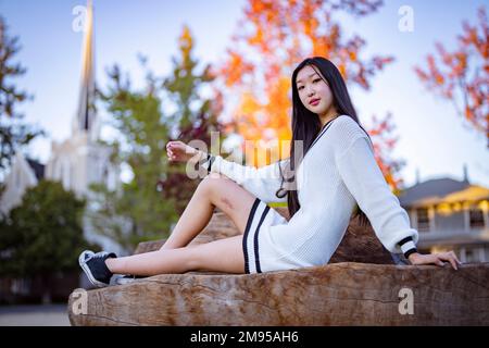 Ragazza adolescente seduta sulla panchina nel Parco Suburban con foglie colorate in autunno e Chiesa Steeple in background Foto Stock