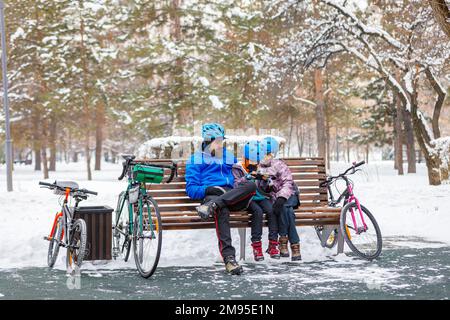 Padre con bambini nel parco invernale. Un uomo con suo figlio e sua figlia riposa dopo il ciclismo. Weekend invernale Foto Stock