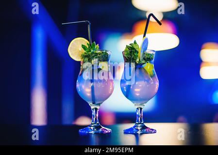 Due bicchieri di cocktail Mojito con cannucce di lime e menta alla festa su sfondo luminoso e sfocato Foto Stock