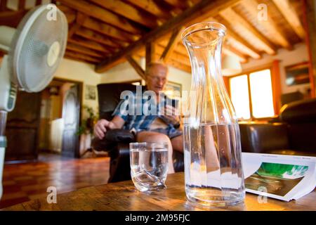 Anziani e ondata di calore: Rimanere idratati. Calore intenso: Vecchio bere acqua e ventilatore soffiare aria. Illustrazione, persone anziane e idratazione, Foto Stock