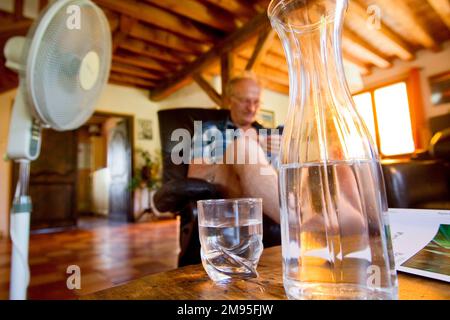 Anziani e ondata di calore: Rimanere idratati. Calore intenso: Vecchio bere acqua e ventilatore soffiare aria. Illustrazione, persone anziane e idratazione, Foto Stock