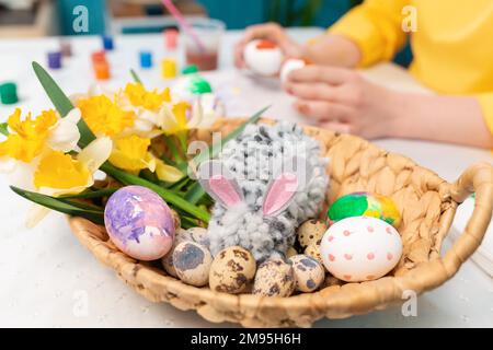 Primo piano del cesto di vimini con un coniglio giocattolo, uova di Pasqua e un narcisi. Concetto di vacanze tradizionali. Foto Stock