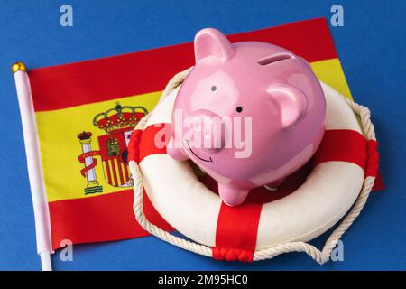 Piggy bank, lifboa e bandiera su sfondo blu, concetto sul tema del salvataggio dell'economia spagnola Foto Stock