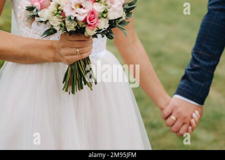 Il bouquet di nozze della sposa di fiori rosa freschi in mano e tenendo le mani con lo sposo. Dettagli matrimonio. Foto Stock