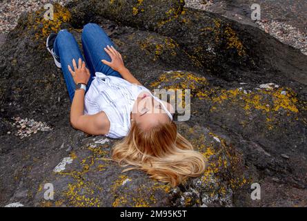 Una bella donna bionda Rhianna Martin dorme sulle rocce mentre si gode il caldo tempo alla spiaggia di Wormit nella contea di Fife, Scozia, Regno Unito Foto Stock