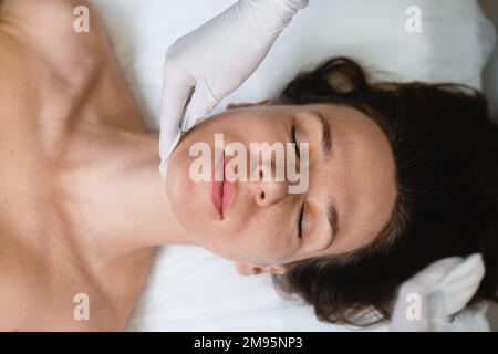 Vista dall'alto del viso femminile rilassante alla mano di bellezza massaggio ringiovanente manuale anti-invecchiamento presso il salone professionale Foto Stock