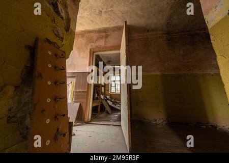 Porta aperta in legno che porta alla sala distrutta dalle intemperie di un edificio abbandonato di luce del giorno Foto Stock
