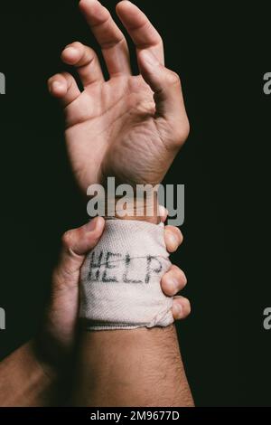 La fine di un dolore è l'inizio di un altro. un uomo irriconoscibile con bende avvolte intorno al polso mostrando aiuto scritto su di esso. Foto Stock