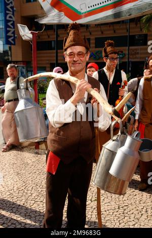 Un gruppo folcloristico del villaggio di Camacha, che visita Funchal, la capitale di Madeira. L'uomo in primo piano sta portando lattine di latte su un bastone di legno equilibrato sulla sua spalla. Foto Stock