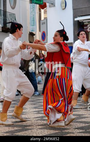 Due membri di un gruppo folcloristico di Gaula, visto qui ballare a Funchal, la capitale di Madeira. La coppia indossa un costume tradizionale, compresi i cappucci neri del cranio con punte. La donna indossa prevalentemente rosso, compresa una gonna a righe lunghe. L'uomo è vestito di bianco. Foto Stock