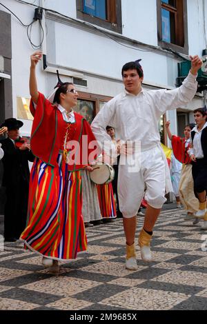 Due membri di un gruppo folcloristico di Gaula, visto qui ballare a Funchal, la capitale di Madeira, con musicisti che suonano sullo sfondo. La coppia indossa un costume tradizionale, compresi i cappucci neri del cranio con punte. La donna indossa prevalentemente rosso, compresa una gonna a righe lunghe. L'uomo è vestito di bianco. Foto Stock