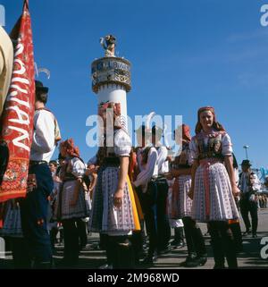 Scena all'Oktoberfest di Monaco, Germania, con persone in costume popolare e la torre della Lowenbrau Brewery sullo sfondo. Foto Stock