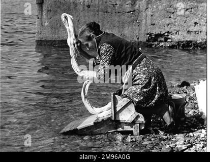 Donna che lava un foglio sul lato di un fiume in Portogallo. Si sta inginocchiando su una piattaforma in legno appositamente progettata, che la impedisce di bagnarsi troppo. Foto Stock