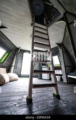 Bianco verticale scale di legno al secondo piano dal soggiorno della casa estiva. Bungalow a forma di piramide dall'interno. Pavimento pareti soffitti scale pazzo Foto Stock