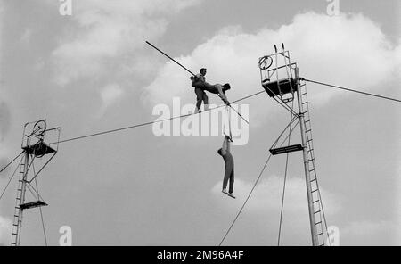 Tre acrobati che fanno un'azione di bilanciamento su un filo alto all'aria aperta. Foto Stock