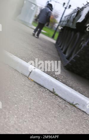 Il bambino piccolo si alza di nuovo vicino al carro armato sulla strada. Lettera Z sullo sfondo sfocato della parete dell'edificio. Foto Stock