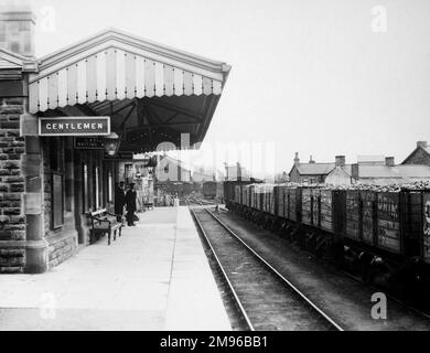 Vista lungo la piattaforma della stazione ferroviaria di Glanamman (o Glanaman) nel Carmarthenshire, Galles del Sud, sulla Great Western Railway. Due del personale della stazione sono visibili in parte lungo la piattaforma e i camion caricati con carbone sono sulla linea a destra. Foto Stock