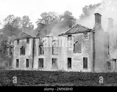 Una grande casa di campagna eviscerata da un incendio, probabilmente nella zona del Galles centrale. L'incendio è recente, in quanto il fumo è ancora in via di deriva dall'edificio. Due delle finestre del piano superiore sono salate, così forse la casa era vuota quando il fuoco ha cominciato. Foto Stock