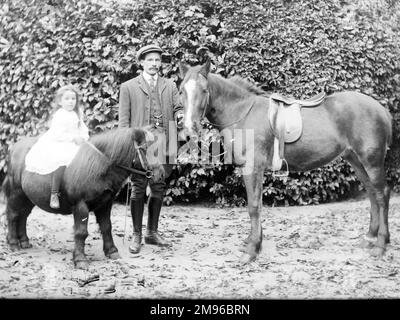 Un padre e una figlia in un giardino, probabilmente da qualche parte nel Galles centrale. Sta in piedi accanto a un piccolo cavallo, tenendo la punta, mentre lei si siede coraggiosamente sul retro di un pony Shetland. Foto Stock